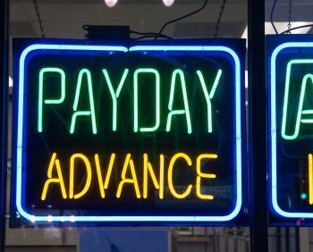 A neon sign reads "PAYDAY ADVANCE" in green and yellow letters, hinting at quick payday loan solutions.