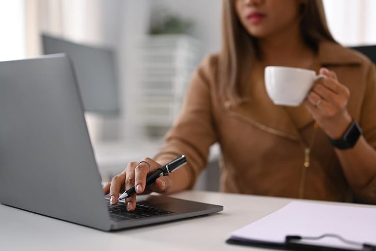 Young female office worker holding coffee cup and checking email on her laptop computer