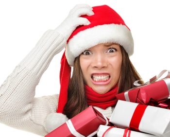 A woman wearing a Santa hat and scarf looks stressed while holding several wrapped gifts, perhaps overwhelmed by the holiday spending.