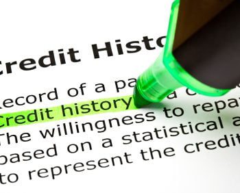 A green highlighter marks the term "Credit history" on a printed document about credit history and its significance in financial assessments, specifically focusing on how tools like a secured credit card can help build or improve one's credit profile.