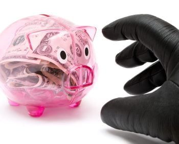 A gloved hand reaches towards a transparent pink piggy bank filled with U.S. dollar bills, symbolizing a charitable donation.