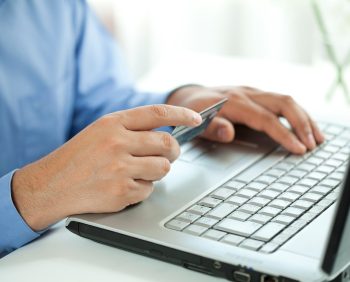 Person in a blue shirt holding a credit card and typing on a laptop keyboard, paying taxes with ease.