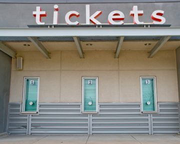 Three closed ticket windows under a sign that reads "tickets" in red letters on a beige and gray wall, standing vigilant against potential ticket scams.