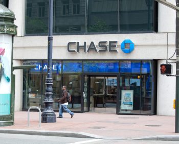 Street view of a Chase bank branch with a pedestrian walking by, located in a city with a visible advertising kiosk labeled "San Francisco" beside the Chase bank entrance.