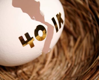 A cracked egg adorned with "401(k)" in gold letters rests in a nest made of straw.