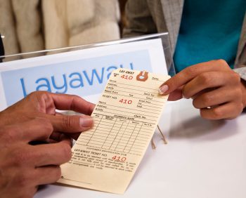 Two people engaging in a layaway transaction, with one person smoothly handing a receipt to the other across the counter.