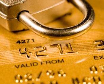 Close-up of a gold credit card partially obscured by a silver padlock, emphasizing security and protection against fraud.