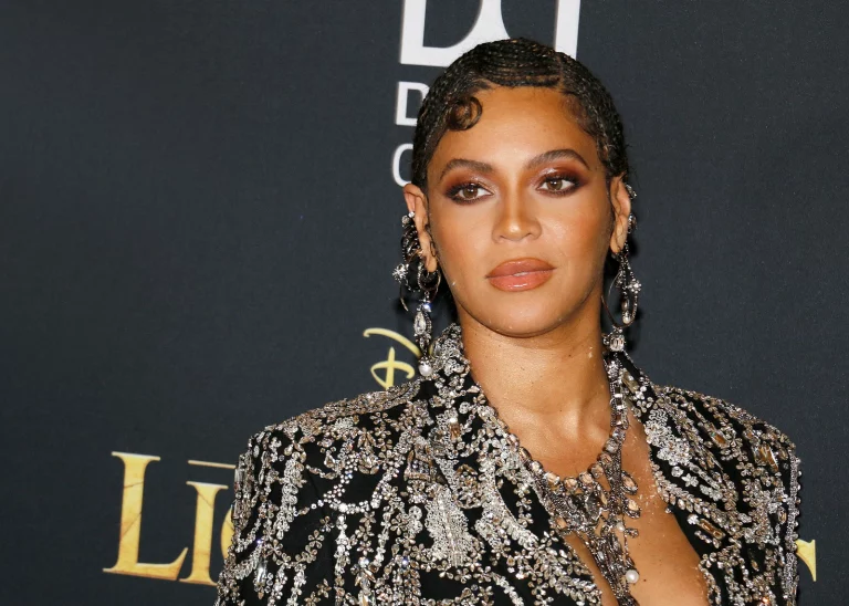 A woman in an ornate, bejeweled outfit stands against a black backdrop adorned with logos and text, embodying the elegance of a financial planner who seamlessly balances credit management and budgeting.