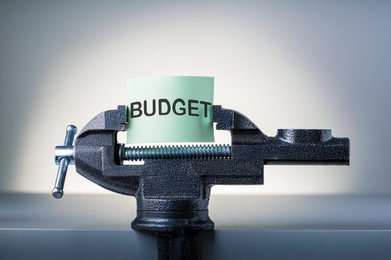 A paper labeled "Budget" is clamped in a black vise, symbolizing the meticulous restraint required by a financial planner to navigate credit challenges.