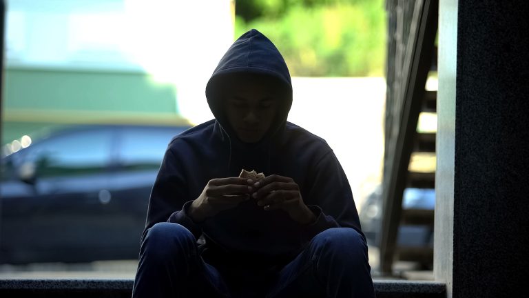 Homeless Hungry Guy Eating Sandwich Sitting In Darkness On Stair