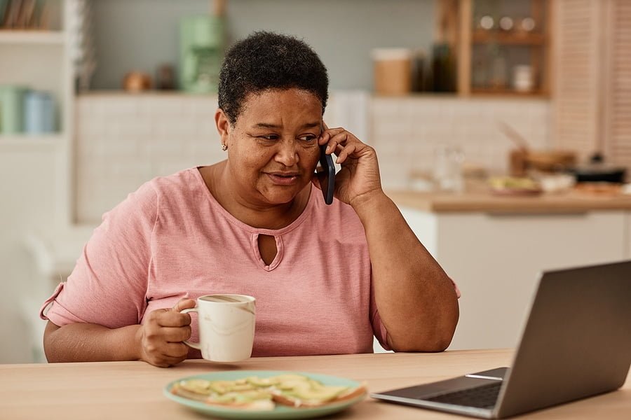 Warm toned portrait of black senior woman talking on phone while enjoying breakfast in morning