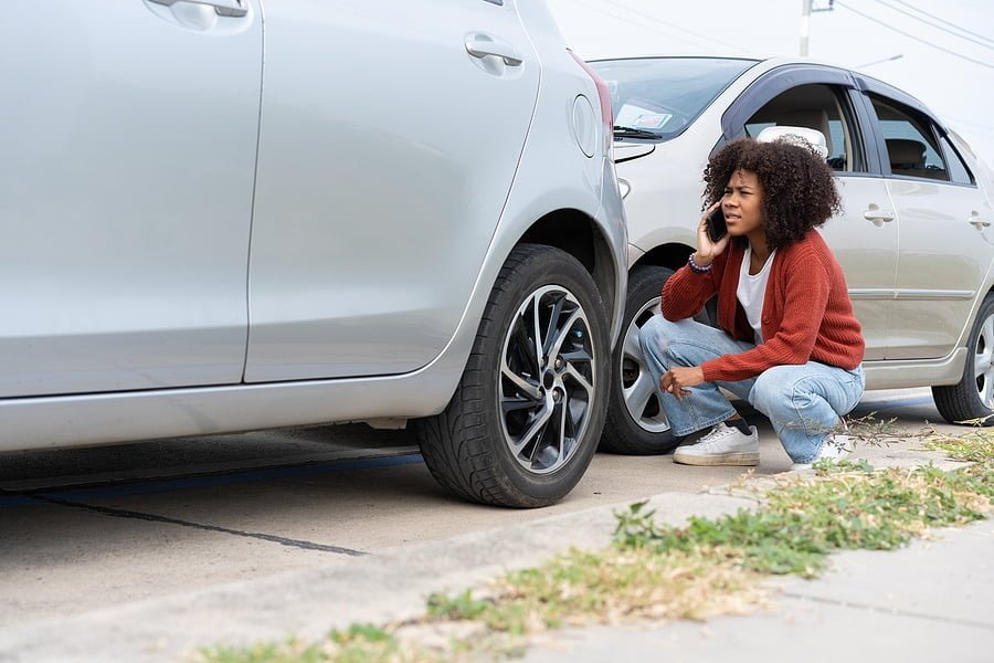 Black women driver check for damage after a car accident before taking pictures and sending insurance. Online car accident insurance claim after submitting photos and evidence to an insurance company.