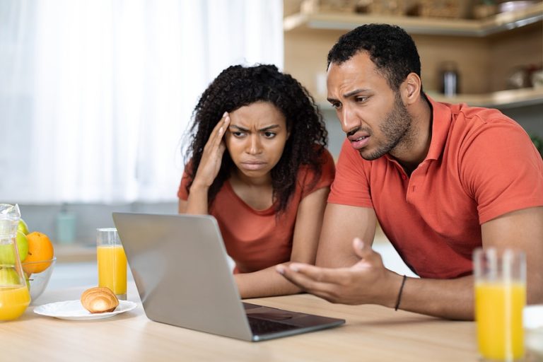 Sad unhappy black female and male in red t-shirts look at computer, have problems with gadget, service and bills