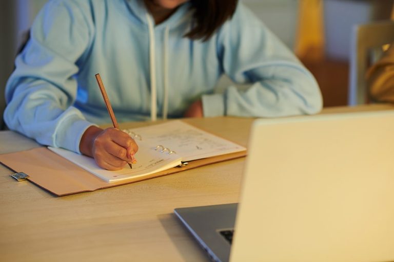 Cropped image of school student writing essay in notebook