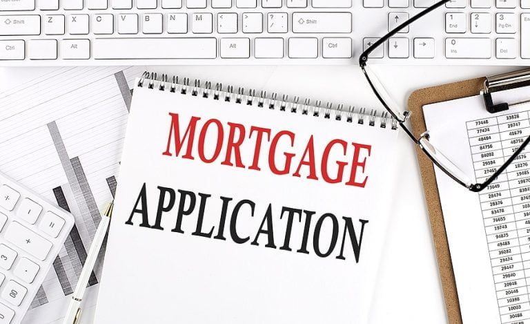 Text MORTGAGE APPLICATION on Office desk table with keyboard, notepad and analysis chart on a white background.