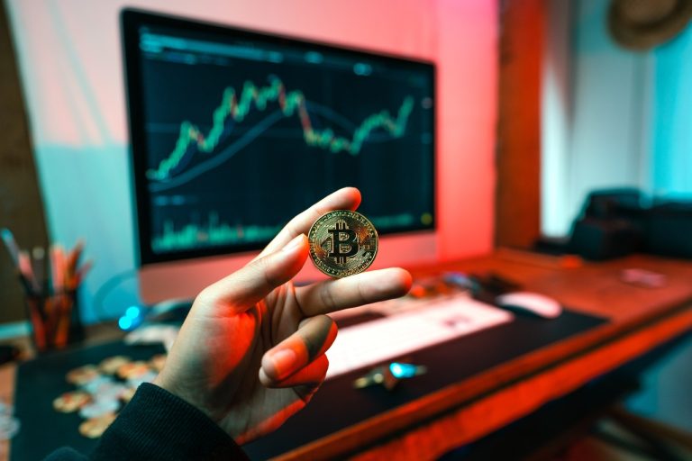 A hand holding a Bitcoin coin appears against a computer screen displaying cryptocurrency market charts, capturing the essence of digital finance and the tools every savvy financial planner needs to design a robust budget.