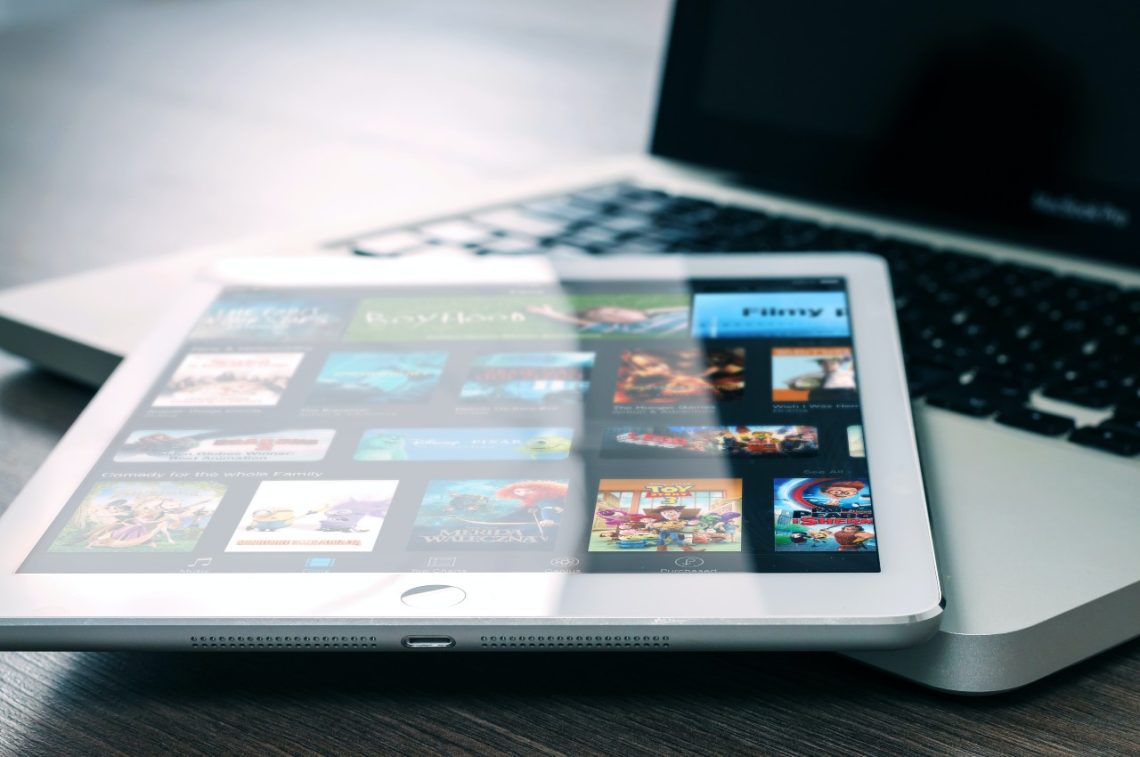 A tablet showcasing various apps and media, including a handy financial planner app, rests on a laptop keyboard atop a wooden surface.