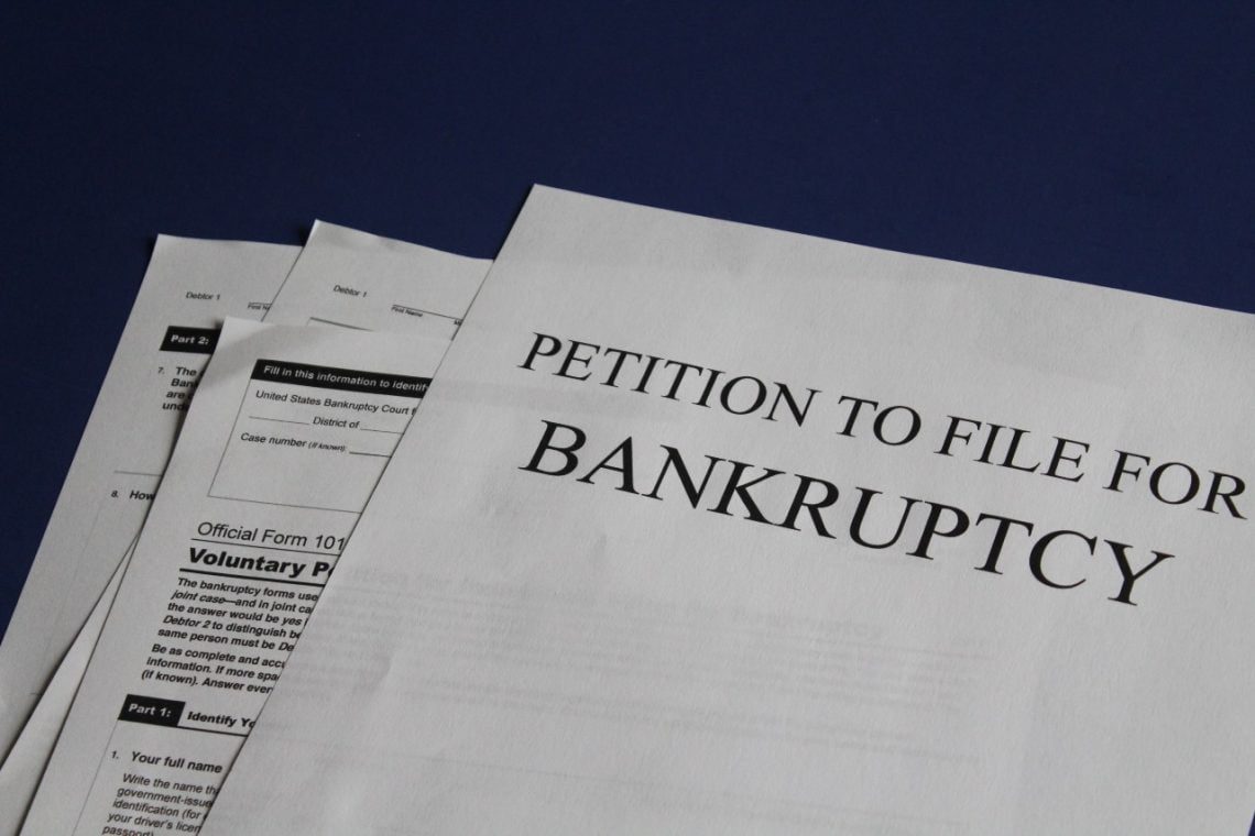 A stack of papers with the top document titled "Petition to File for Bankruptcy" lies next to a credit report that's marked with red flags.