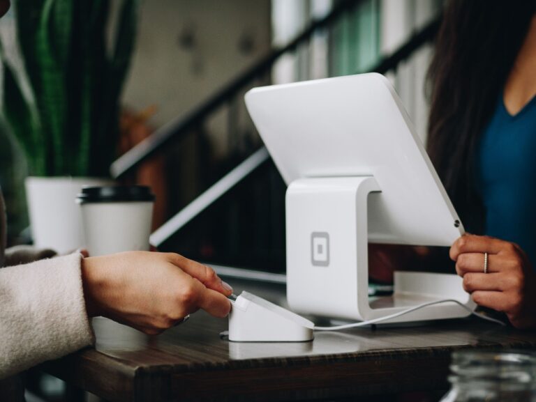 A person makes a payment using a card reader at the checkout counter, with a coffee cup nearby, ensuring their budget aligns thanks to strategic advice from their financial planner.