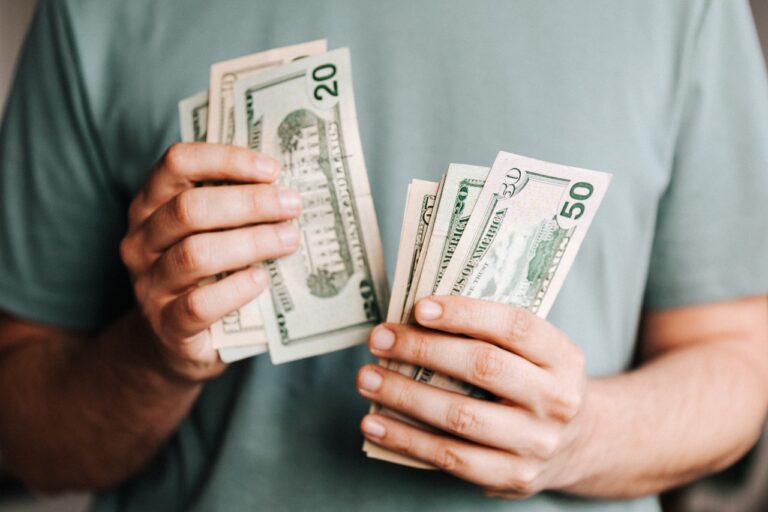 A person in a green shirt meticulously counts US dollar bills, including twenties and fifties, demonstrating keen financial planning skills.