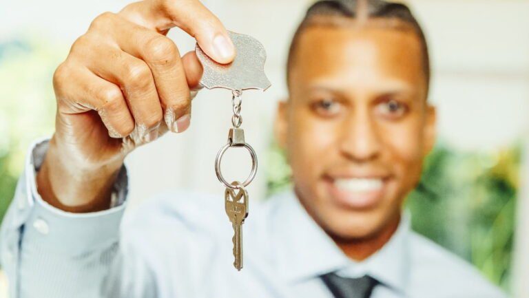 Person holding a key attached to a keyring, smiling at the camera like they've just unlocked a door to budget-friendly living.