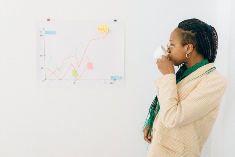 A person in a plaid suit, likely a financial planner, sips from a cup while studying a line graph on the wall.