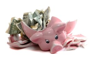 A shattered pink piggy bank, once a symbol of savings, now lies broken with crumpled U.S. dollar bills spilling out—an unmistakable reminder that without a proper budget, financial stability can quickly crumble.