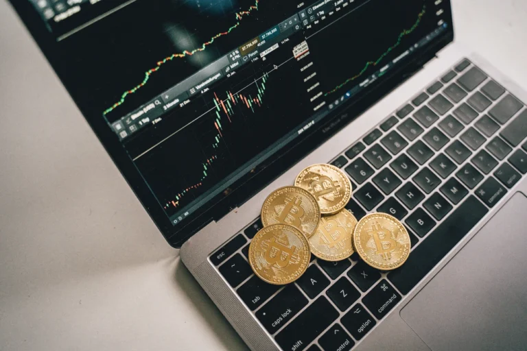 A laptop displaying stock charts sits on a keyboard adorned with four Bitcoin tokens, capturing the essence of a savvy financial planner's workspace.