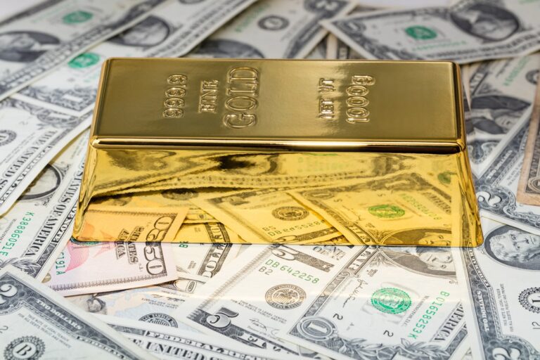 A gold bar gleams atop a pile of U.S. dollar bills, reflecting the meticulous budgeting strategy advised by a seasoned financial planner.