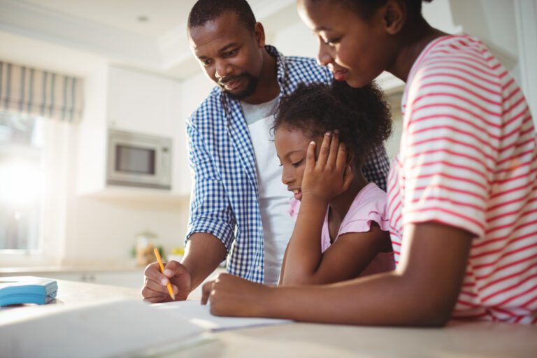 A family of three works on a homework assignment together at the kitchen counter, seamlessly weaving in a lesson on budgeting strategies.