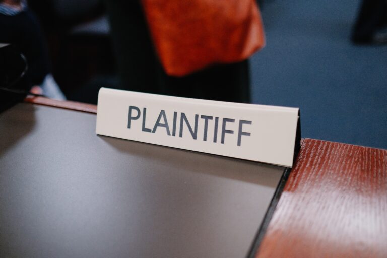 A sign reading "PLAINTIFF" sits on a table surface, as though awaiting a financial planner to guide the case on credit matters.