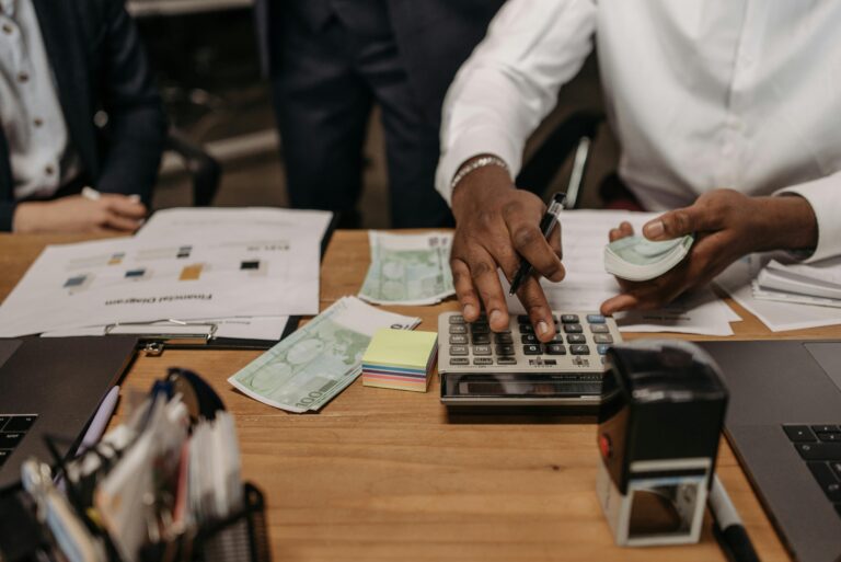 A financial consultant calculating and managing finances at a desk, surrounded by documents, stacks of cash, and office tools.