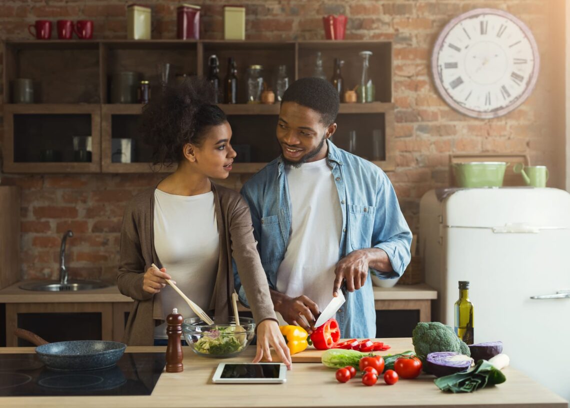 A happy couple preparing vegetables and salad together in a well-organized kitchen, showcasing a healthy food landscape.