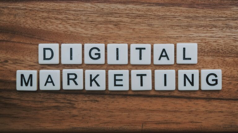 White letter tiles spelling out "DIGITAL MARKETING" arranged in two rows on a wooden table surface, emphasizing the key to get your small business found online.