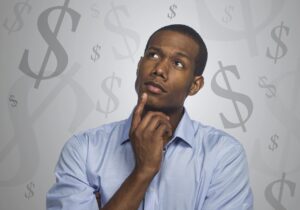 Person in a blue shirt holds chin with a thoughtful expression against a background of dollar signs.