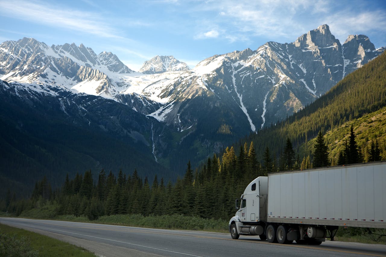 White semi-truck driving through a scenic mountainous highway, illustrating key strategies for running a successful trucking business in the USA.