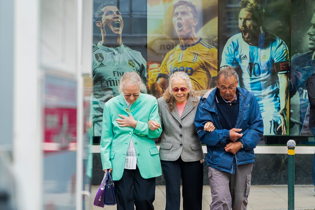 Three elderly people stroll together, arm in arm, in front of a wall adorned with large posters of soccer players in action, seamlessly enjoying their companionship and the security that comes with reliable social security benefits.