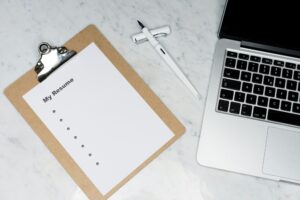 A clipboard with a blank resume sits next to a pen and a laptop on the marble surface, ready for your professional details.