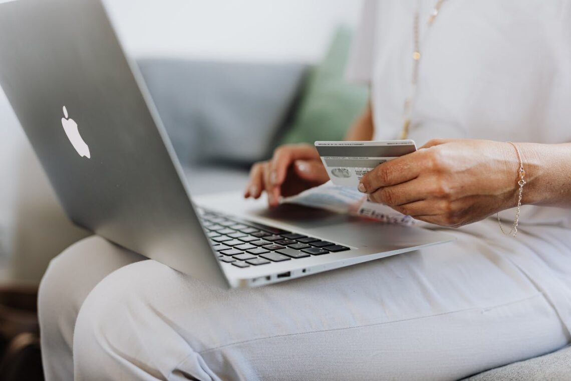 Person seated using a laptop, holding a credit card and an open book, exemplifying secure e-commerce practices during online shopping or bill payment.