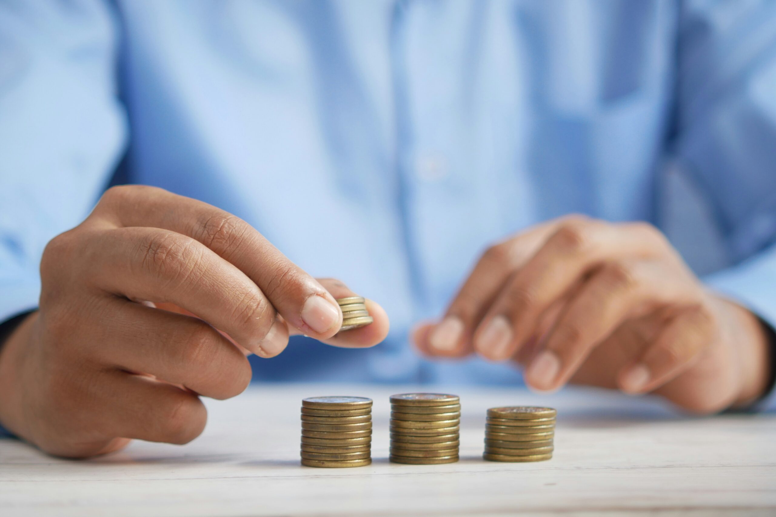 A person in a blue shirt carefully stacks coins into small piles on a white surface, illustrating the benefits of maintaining good credit through disciplined savings.